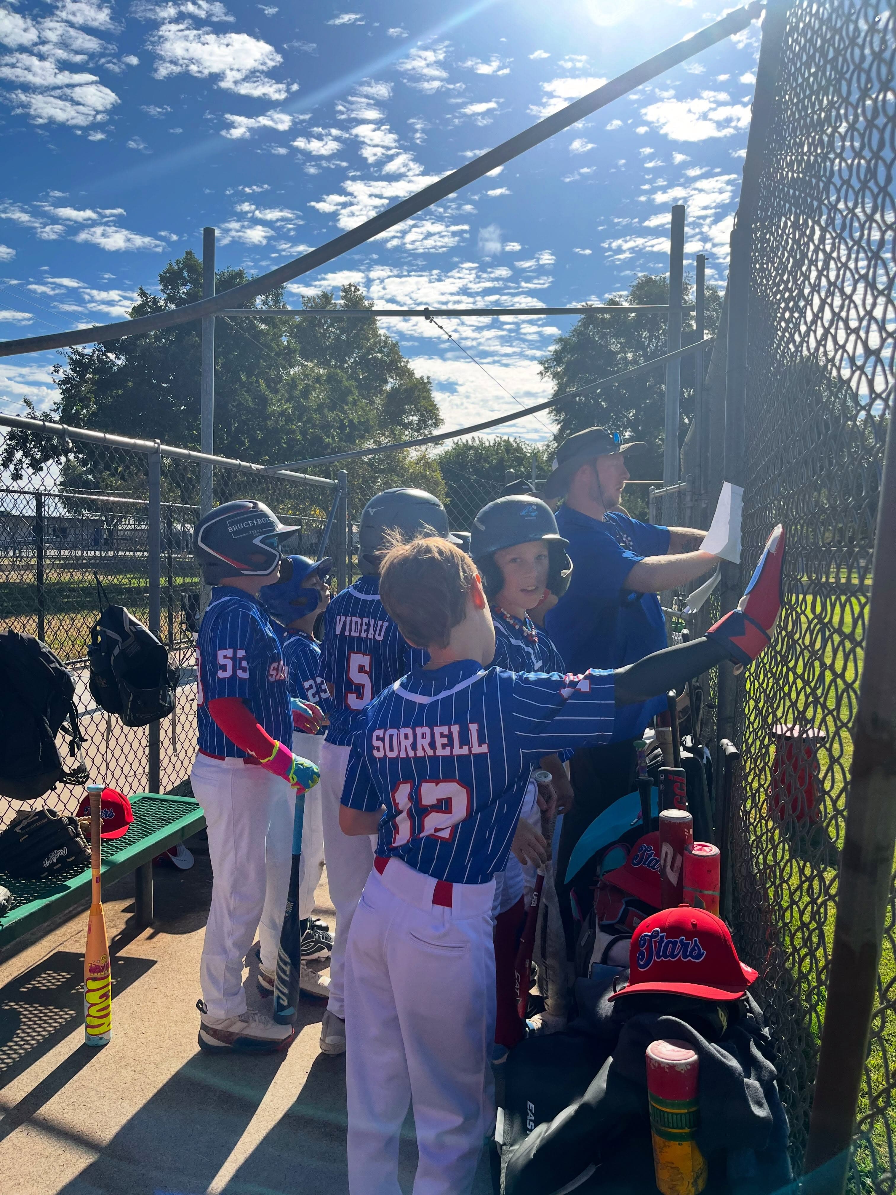 Players in pinstripe jerseys talk with a coach in the dugout.