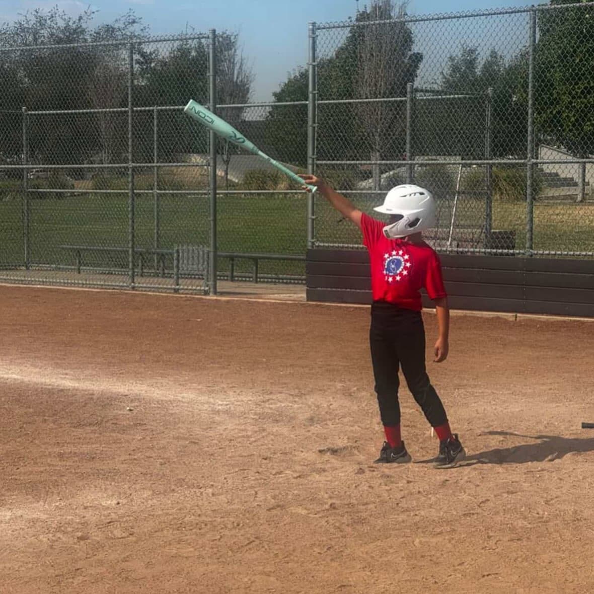 A young player in a red Stars shirt raises a bat on the infield at Wild Rose Park.