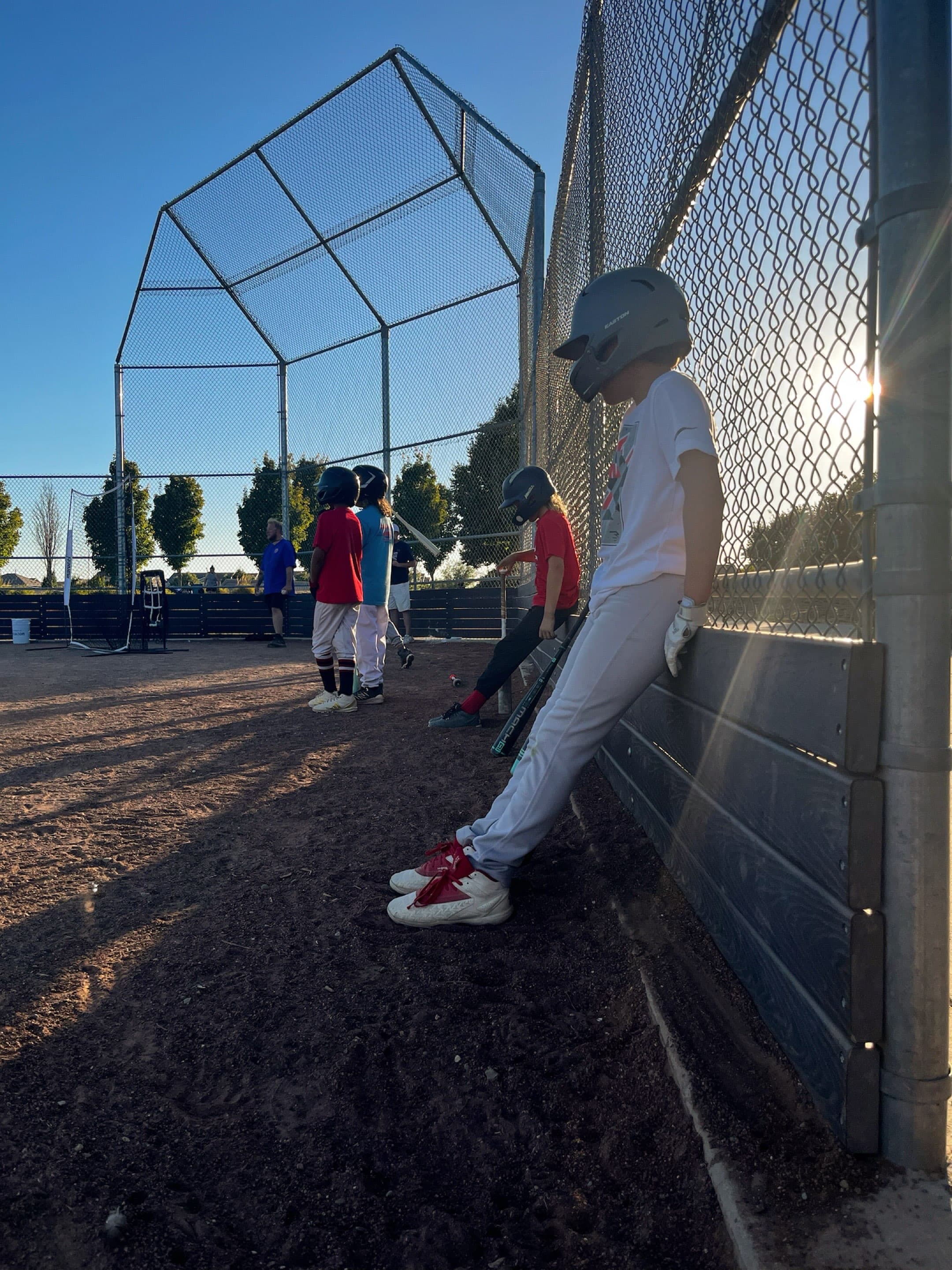 A Stars player in a helmet leans against the backstop at Wild Rose Park while teammates wait on the dirt.